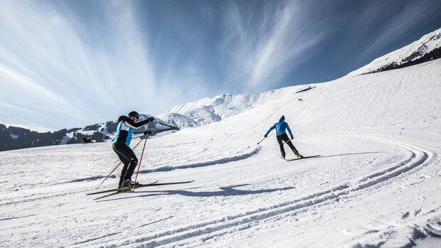 Zwei Skifahrer auf der Piste im Gegenlicht